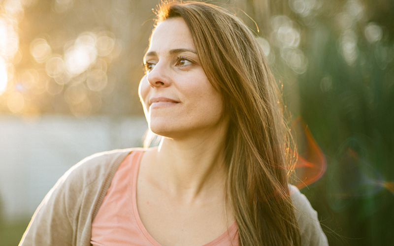 A side view of a woman looking in the distance with the sunlights glow behind her.